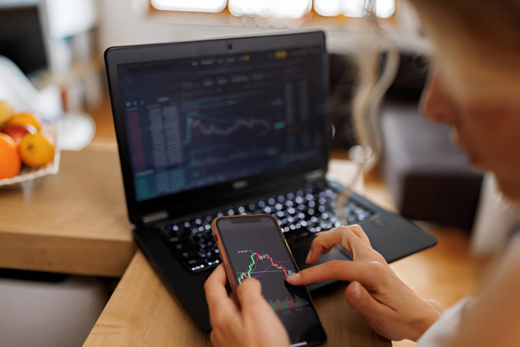 woman checking stock markets on a phone and a laptop