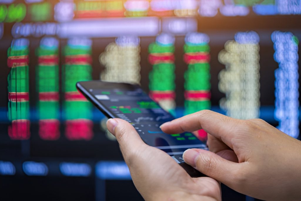 close-up of a man checking stock markets on a phone and a computer