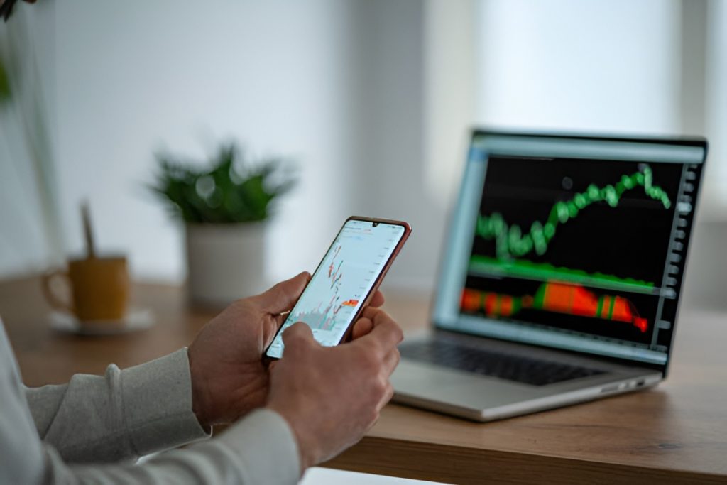 man checking stock markets on a phone and a laptop